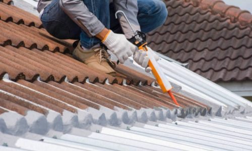 Technician man hand using glue gun with silicone adhesive or manual caulking gun with polyurethane to seal the leak on the roof. Installing and building construction concept.