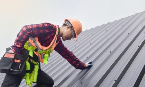 Roofer worker in protective uniform wear and gloves,Roofing tools,installing new roofs under construction,Electric drill used on new roofs with metal sheet.